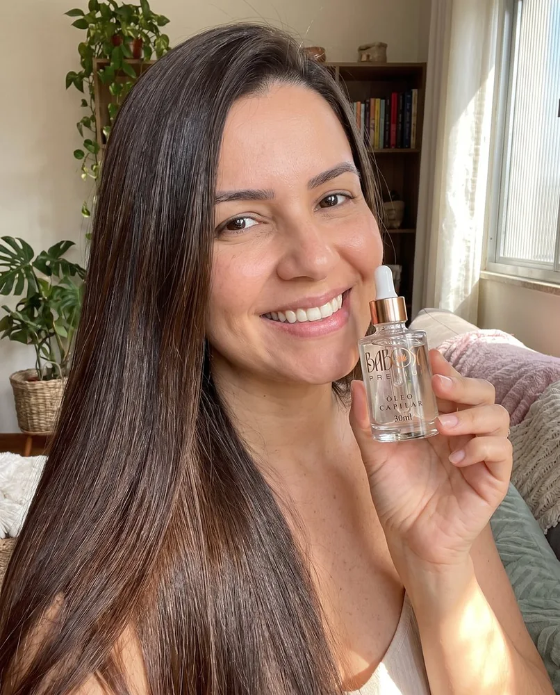 Mulher sorrindo com cabelo liso brilhante segurando o frasco de Babosa Premium