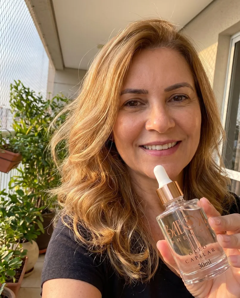 Mulher de cabelo loiro ondulado na varanda com o frasco de Babosa Premium